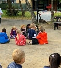 Børn og pædagoger sidder på Birkelys legeplads, og venter på flødeboller.